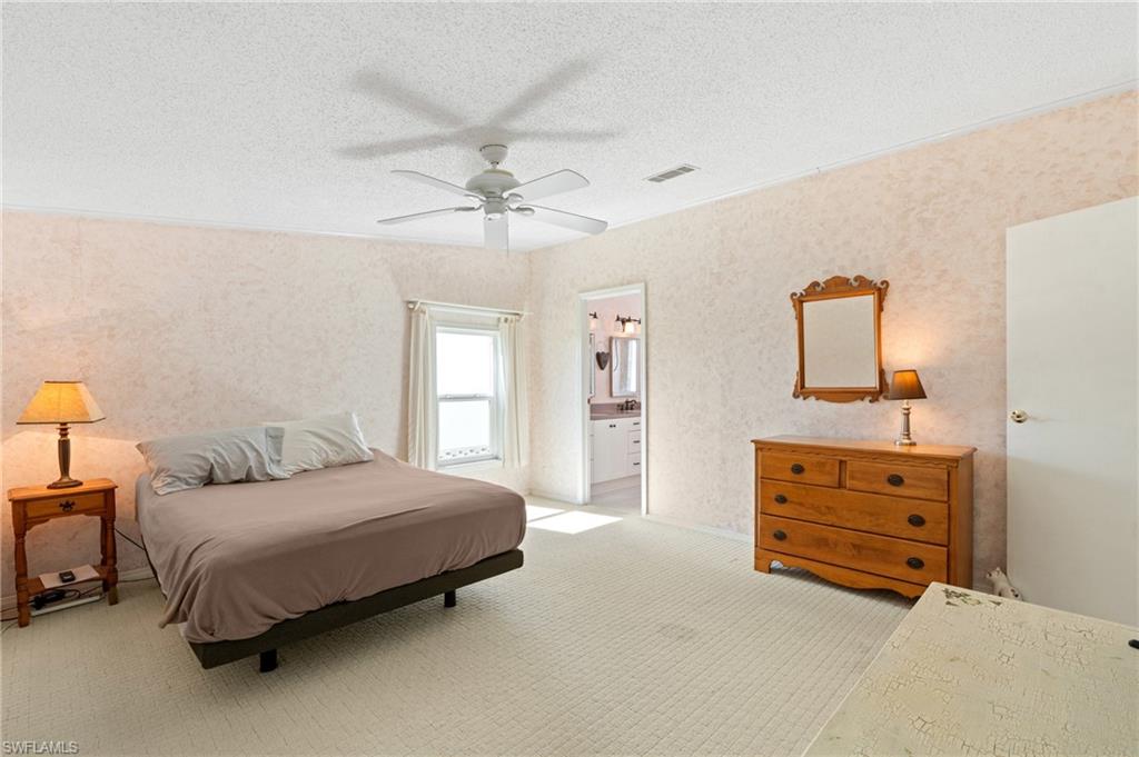 278 Riverwood Road Naples, FL 34114 - Photo 20 of 43 Bedroom with visible vents, a ceiling fan, a textured ceiling, connected bathroom, and light colored carpet