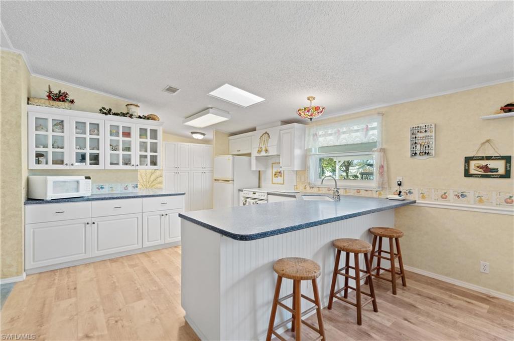 278 Riverwood Road Naples, FL 34114 - Photo 5 of 43 Kitchen featuring light wood-style flooring, white appliances, a kitchen bar, and a peninsula