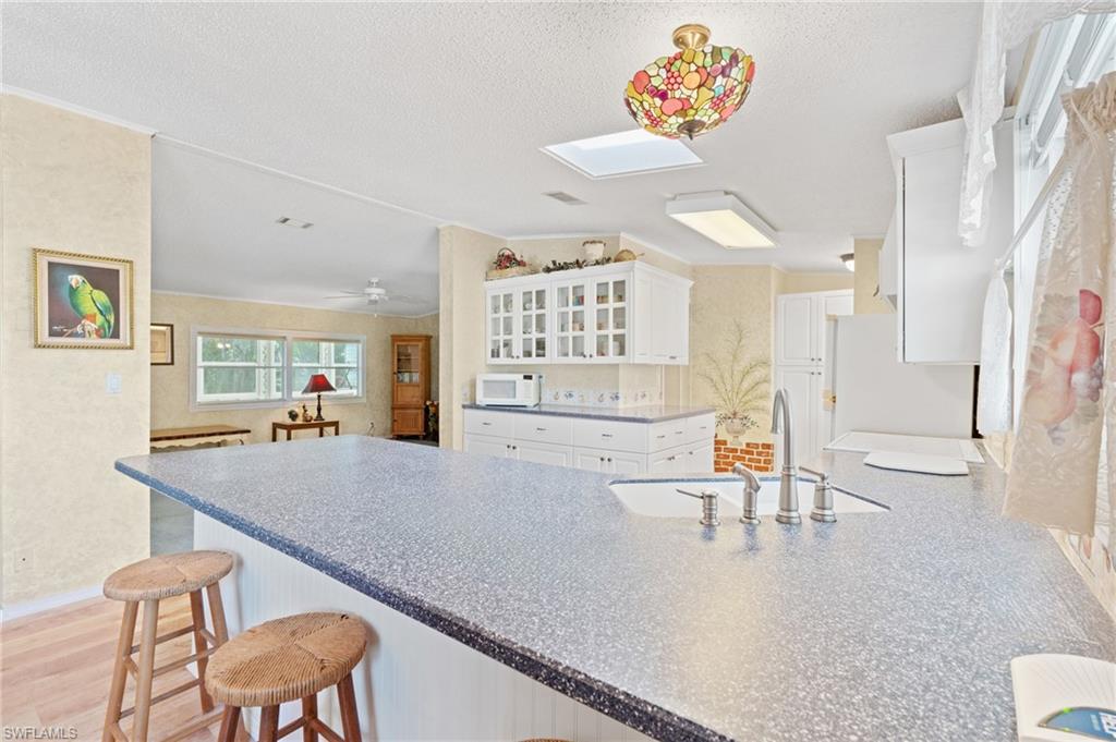 278 Riverwood Road Naples, FL 34114 - Photo 6 of 43 Kitchen with lofted ceiling with skylight, a sink, white appliances, white cabinets, and glass insert cabinets