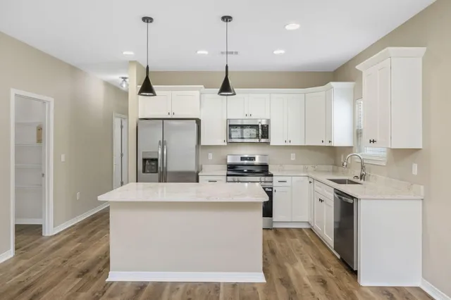 a kitchen with stainless steel appliances granite countertop a sink a stove a refrigerator and white cabinets with wooden floor