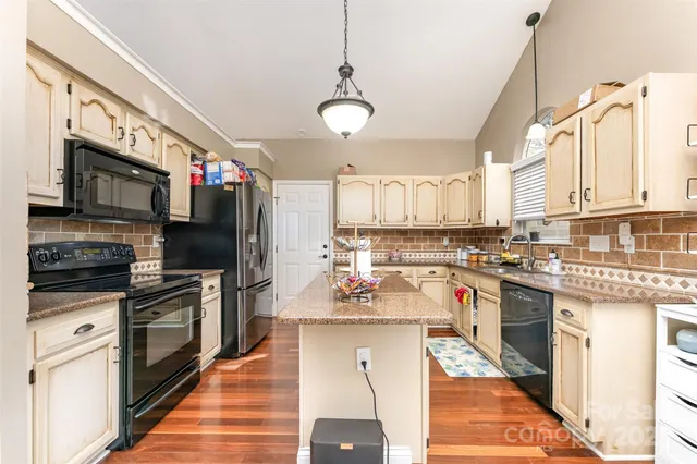 a kitchen with stainless steel appliances granite countertop a refrigerator a stove top oven a sink dishwasher and white cabinets with wooden floor