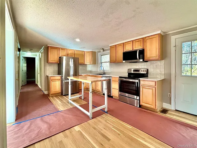 a kitchen with stainless steel appliances kitchen island granite countertop a refrigerator oven a sink dishwasher and white cabinets with wooden floor