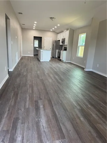 an empty room with wooden floor and a kitchen