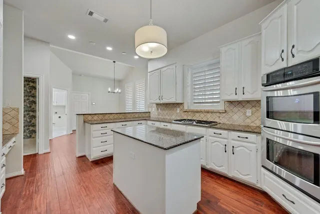 a kitchen with stainless steel appliances granite countertop a stove top oven a sink dishwasher and a microwave oven on the wooden floor