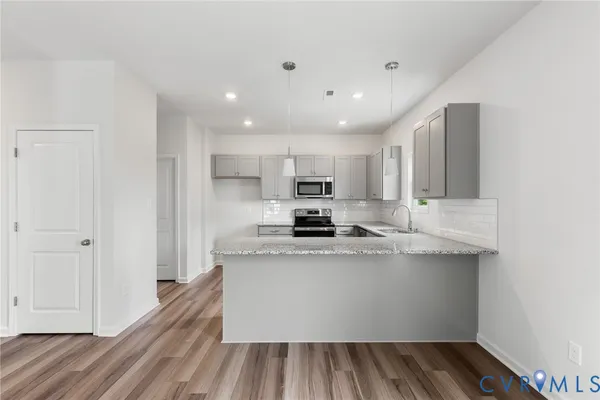 a view of a kitchen with kitchen island a sink wooden floor and stainless steel appliances