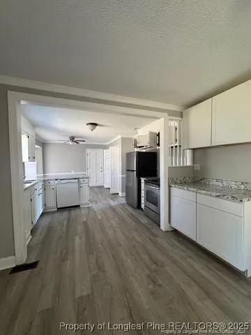 a kitchen with granite countertop a refrigerator oven a sink dishwasher and white cabinets with wooden floor