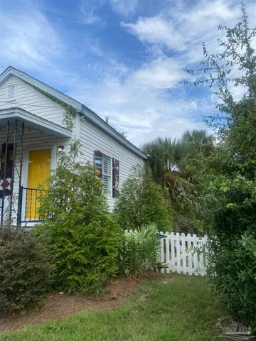 a view of a house with brick walls and a yard with plants and large trees