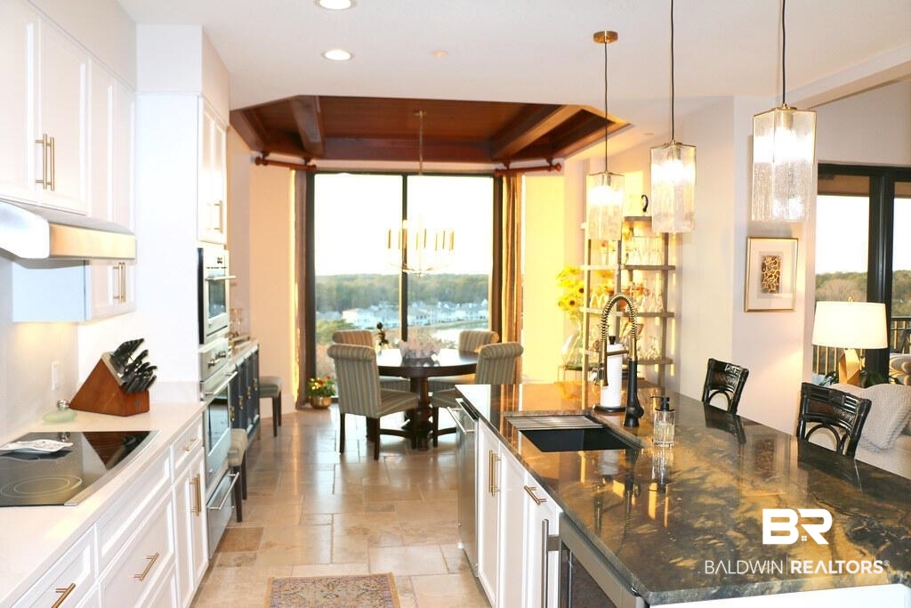 18269 Colony Drive, Unit 803 Fairhope, AL 36532 - Photo 5 of 27 Kitchen with white cabinets, stone tile flooring, decorative light fixtures, dark stone counters, and a kitchen breakfast bar