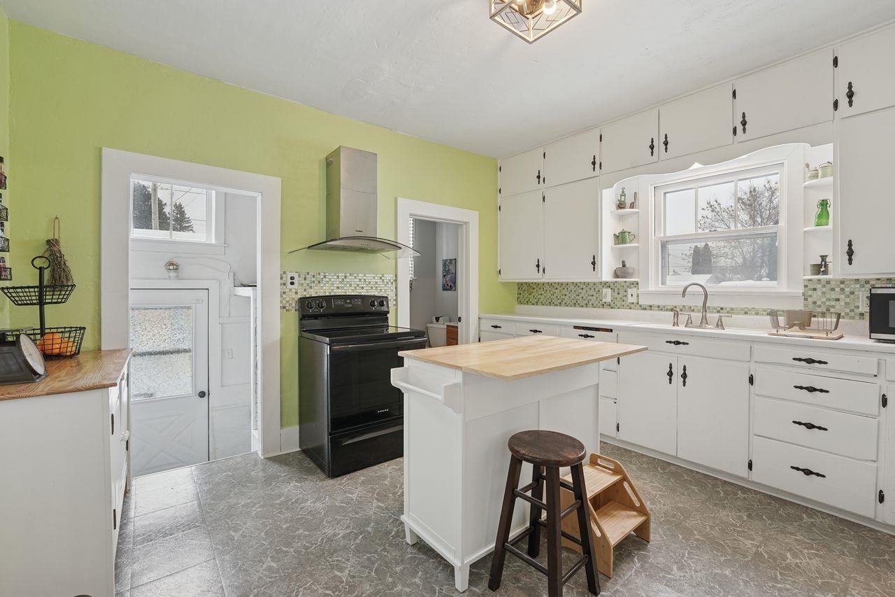 802 3rd Avenue East Ashland, WI 54806 - Photo 7 of 22 Kitchen with open shelves, black range with electric stovetop, butcher block counters, a kitchen bar, and wall chimney exhaust hood