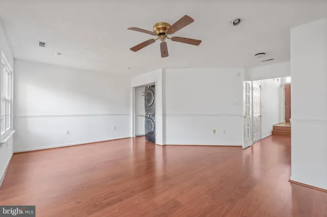 a view of an empty room with wooden floor and a ceiling fan