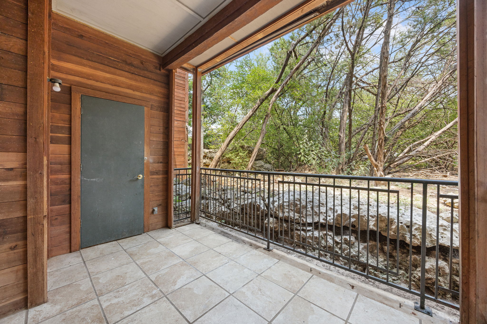 4711 Spicewood Springs Road, Unit 1106 Austin, TX 78759 - Photo 14 of 19 Covered outdoor patio featuring extensive wood paneling, tiled flooring, dark metal railing, and rock landscaping