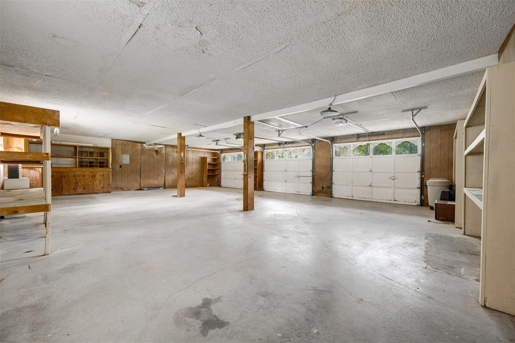 8798 Hill N Dale Road Tyler, TX 75709 - Photo 24 of 31 Spacious garage featuring a concrete floor, two white overhead garage doors with window inserts, exposed structural beams, and built-in shelving and cabinetry for storage