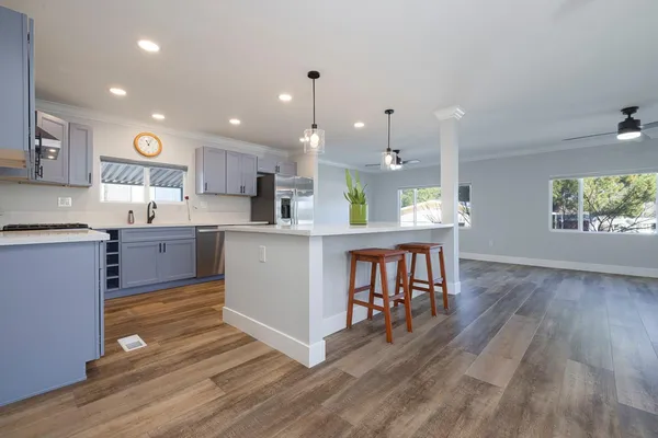 a kitchen with stainless steel appliances granite countertop a stove top oven a sink dishwasher a dining table and chairs with wooden floor