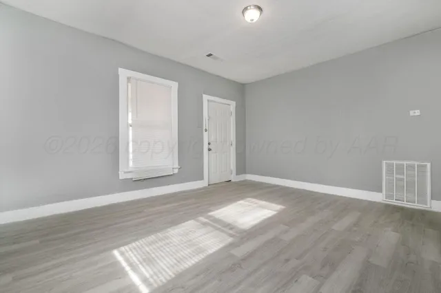 a view of an empty room with wooden floor and a window