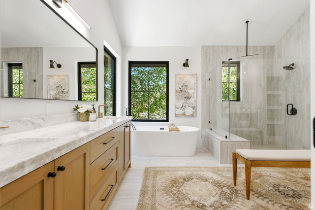 3027 Homestead Road Park City, UT 84098 - Photo 25 of 62 Spacious bathroom featuring a double vanity with light wood cabinetry and a marble-look countertop, an oval freestanding soaking tub, a frameless glass shower with a built-in bench, and multiple windows with black trim