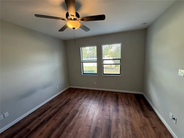 an empty room with wooden floor chandelier fan and windows