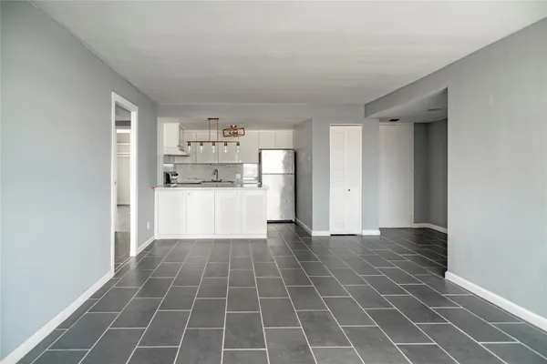 a view of an empty room with kitchen and window