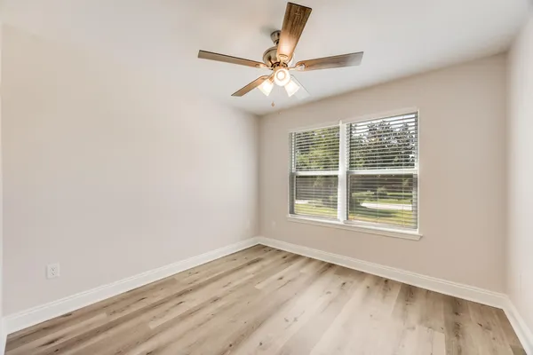 an empty room with wooden floor fan and windows
