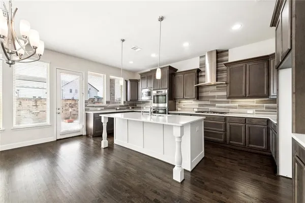 a kitchen with stainless steel appliances granite countertop a stove a sink dishwasher a refrigerator white cabinets and wooden floor next to a window