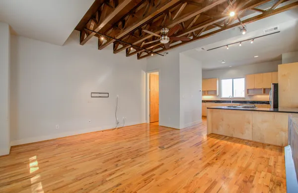a view of empty room with wooden floor and kitchen view