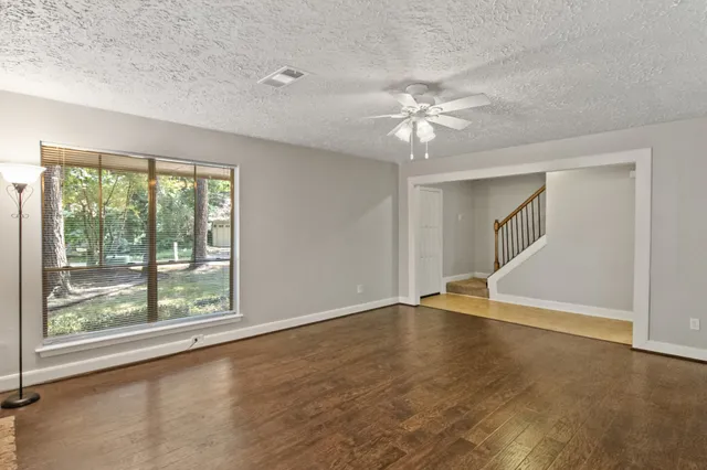 an empty room with wooden floor fan and windows
