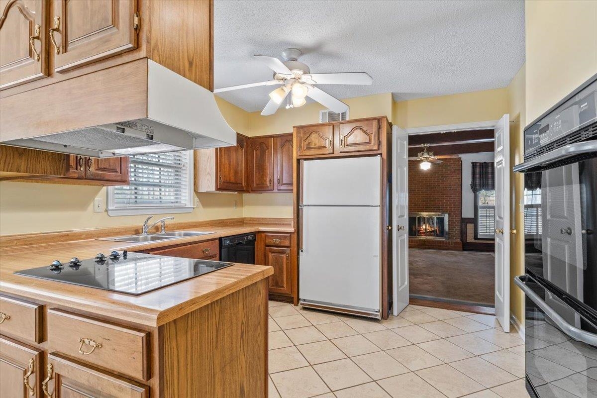 2587 McVay Road Memphis, TN 38119 - Photo 14 of 35 Kitchen with black appliances, a ceiling fan, a brick fireplace, light countertops, and a textured ceiling
