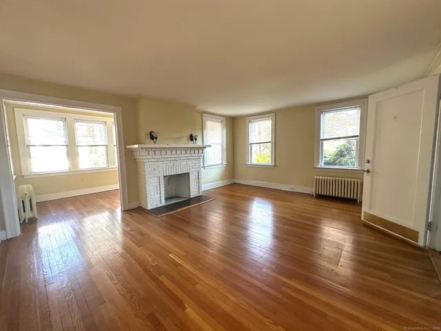 an empty room with wooden floor fireplace and windows