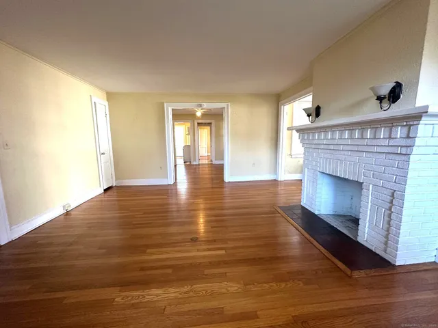 a view of an empty room with wooden floor fireplace and a window
