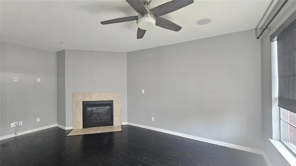 an empty room with wooden floor a ceiling fan a fireplace and windows