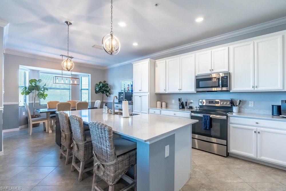 9578 Trevi Court, Unit 5142 Naples, FL 34113 - Photo 3 of 49 a large kitchen with stainless steel appliances granite countertop a stove a sink a microwave a dining table and chairs