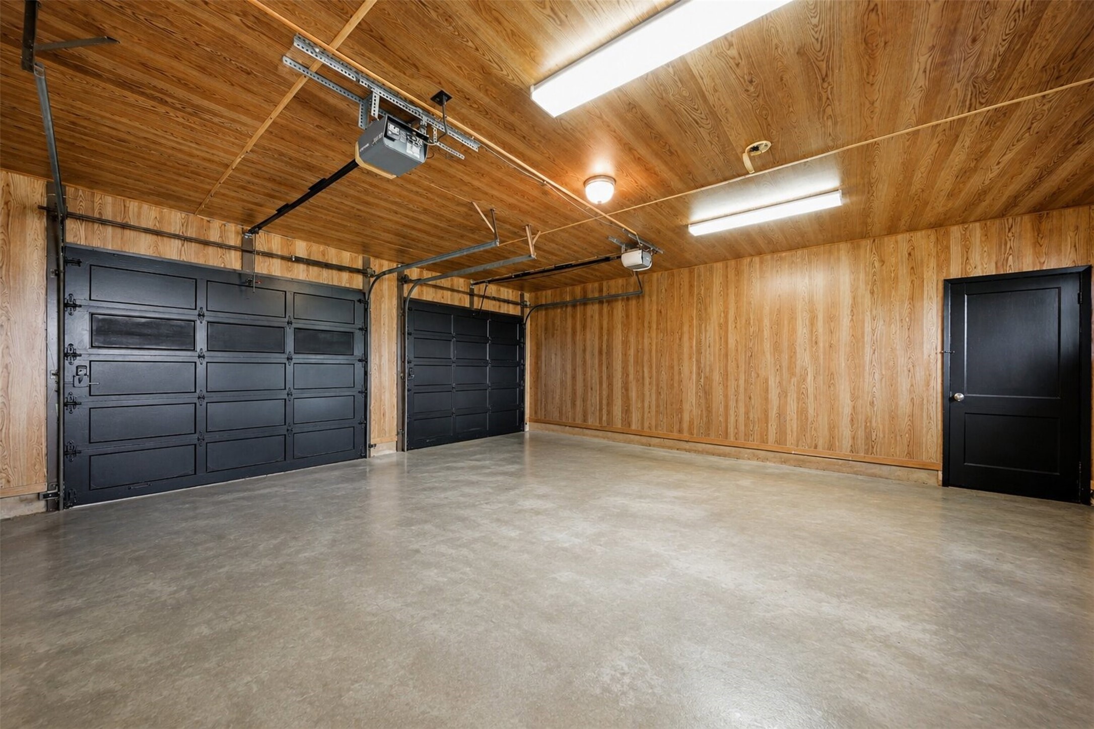 5443 Randon School Road Rosenberg, TX 77471 - Photo 18 of 20 Spacious garage with concrete flooring, wood-paneled walls and ceiling, overhead lighting, black garage doors, and exterior access door.