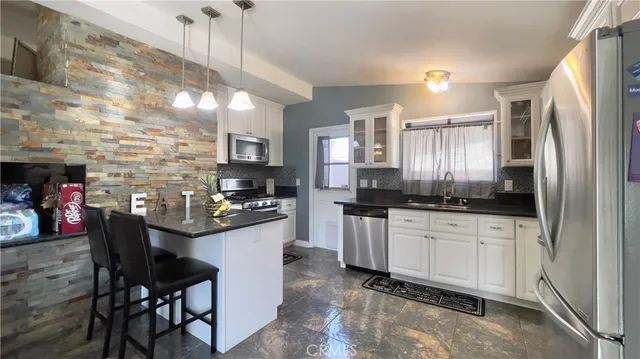 a kitchen with stainless steel appliances granite countertop a sink a stove a refrigerator cabinets and a dining table