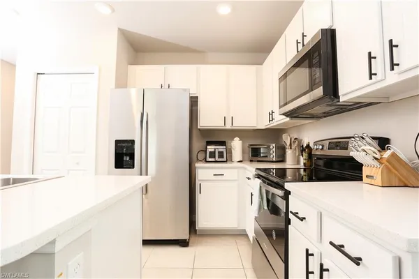 a kitchen with stainless steel appliances granite countertop a stove a sink a microwave a refrigerator and white cabinets with wooden floor