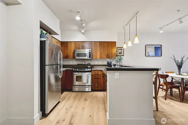 a kitchen with stainless steel appliances granite countertop a refrigerator a stove a sink a dining table and chairs with wooden floor