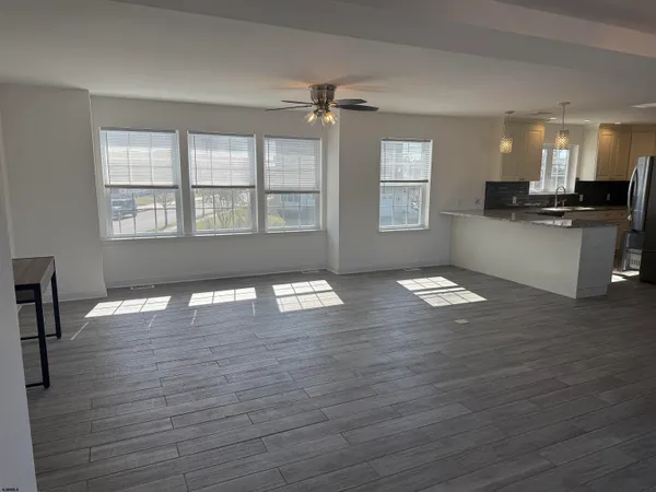 a view of an empty room with kitchen and wooden floor