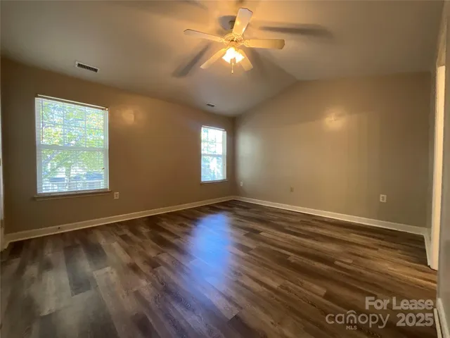 a view of an empty room with wooden floor and a ceiling fan