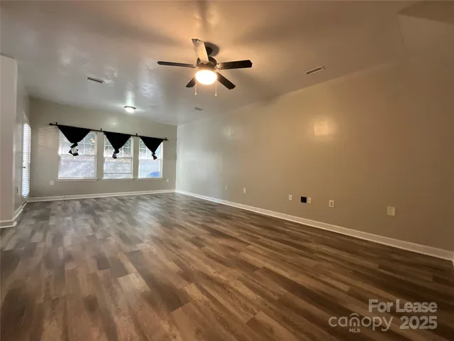 an empty room with wooden floor fan and windows