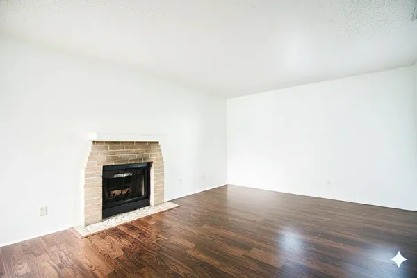 a view of an empty room with wooden floor and a fireplace