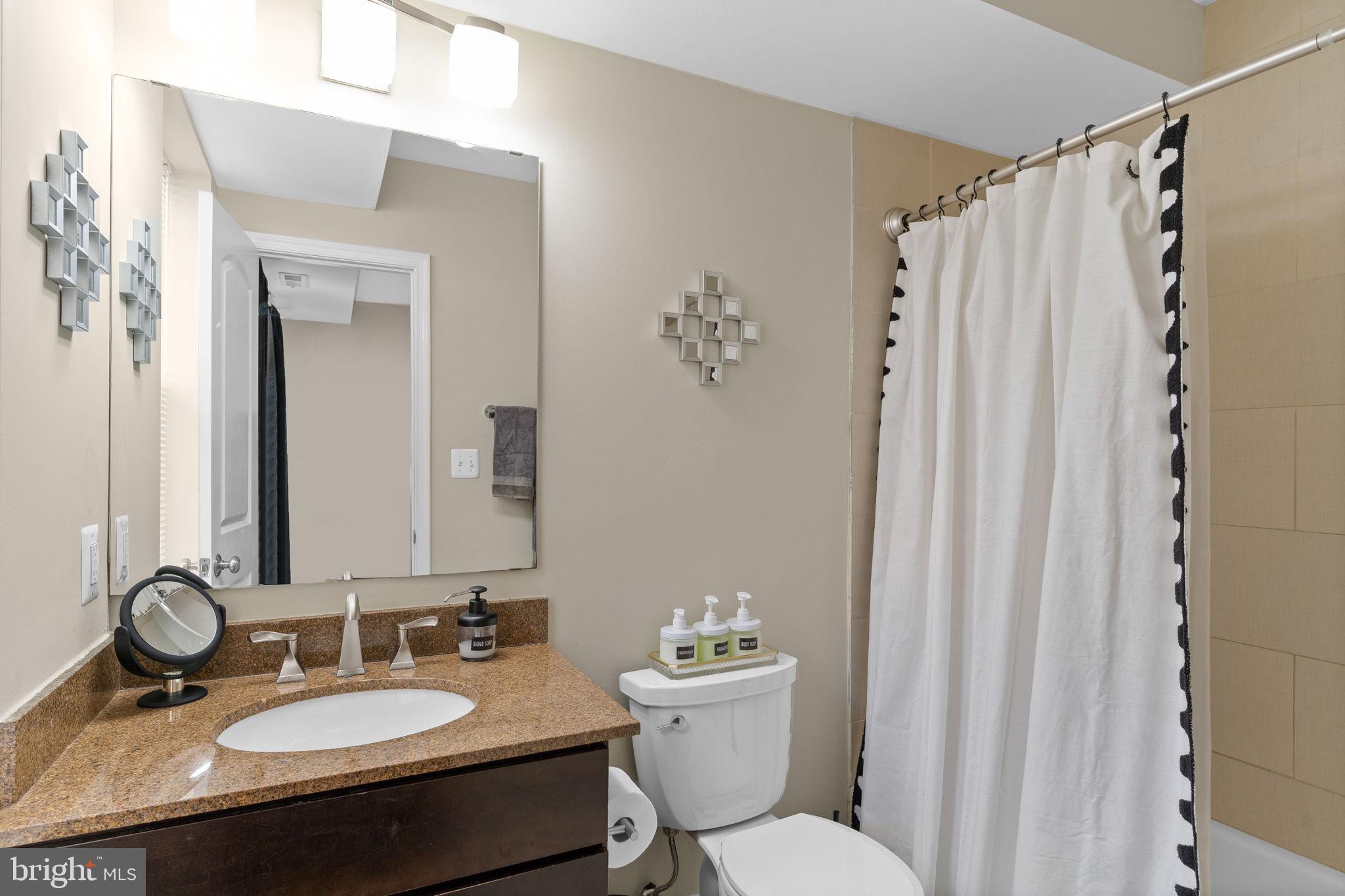 417 18th Street Northeast, Unit 103 Washington, DC 20002 - Photo 30 of 40 a bathroom with a granite countertop sink toilet a mirror a vanity and shower