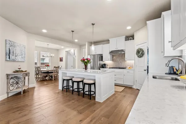 a large white kitchen with stainless steel appliances granite countertop a stove a sink a dining table and chairs with wooden floor