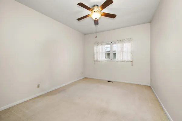 an empty room with chandelier fan and windows