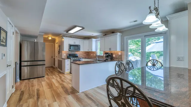 a kitchen with stainless steel appliances granite countertop a refrigerator a stove a sink dishwasher a dining table and chairs with wooden floor