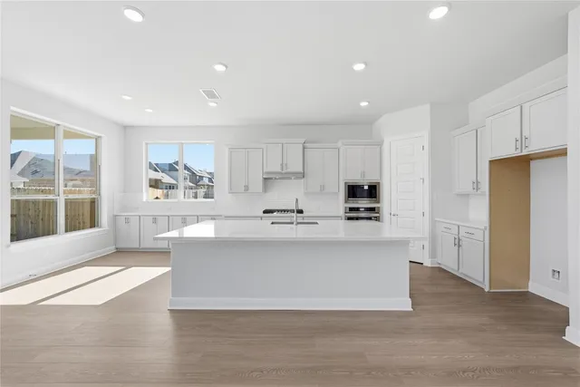 a large white kitchen with kitchen island a sink a center island stainless steel appliances and a window