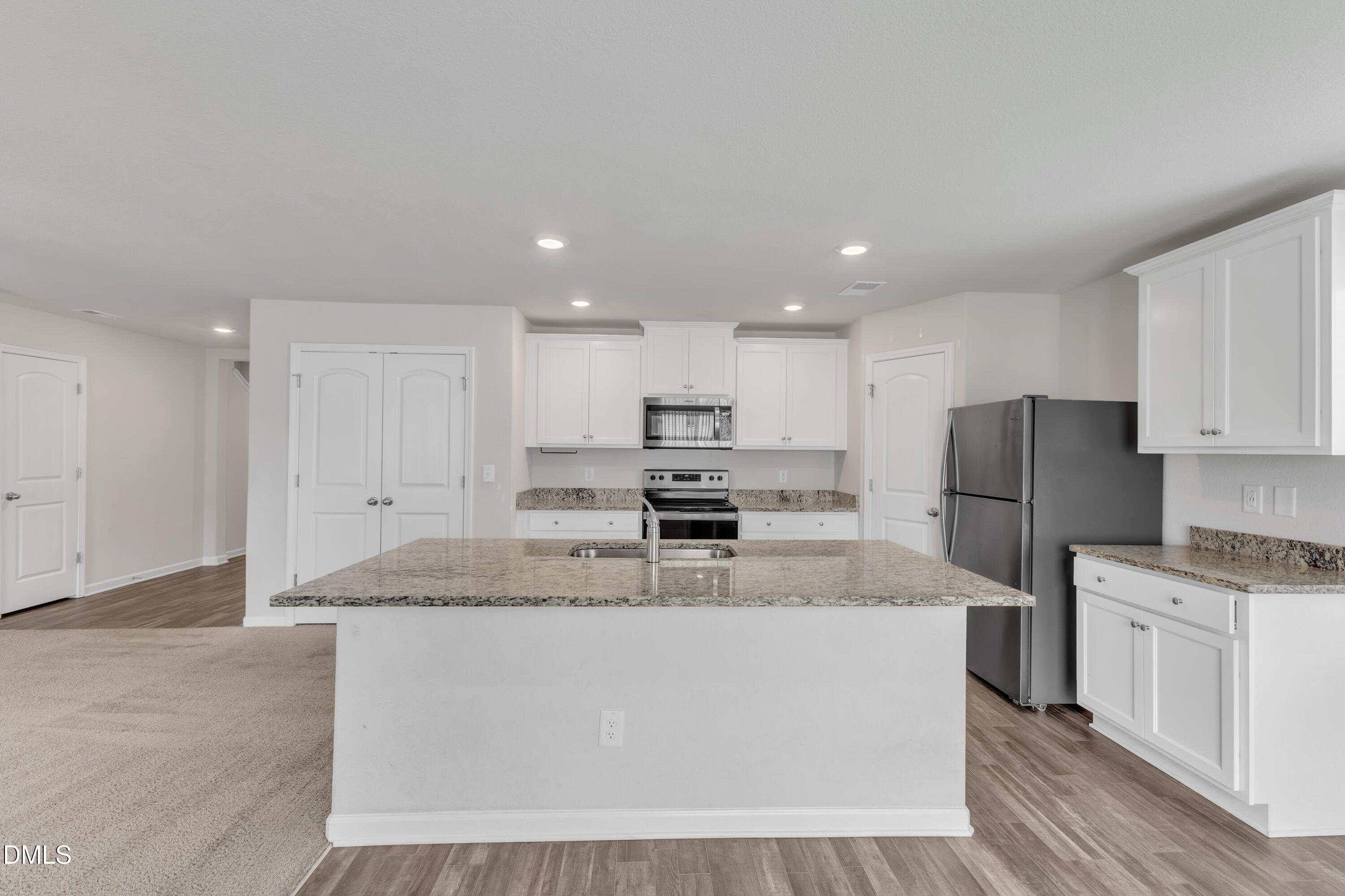 717 Little Patch Street Zebulon, NC 27597 - Photo 13 of 36 a large kitchen with stainless steel appliances granite countertop a stove a sink a refrigerator and white cabinets with wooden floor
