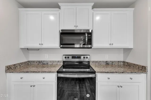 a kitchen with granite countertop white cabinets and a stove top oven