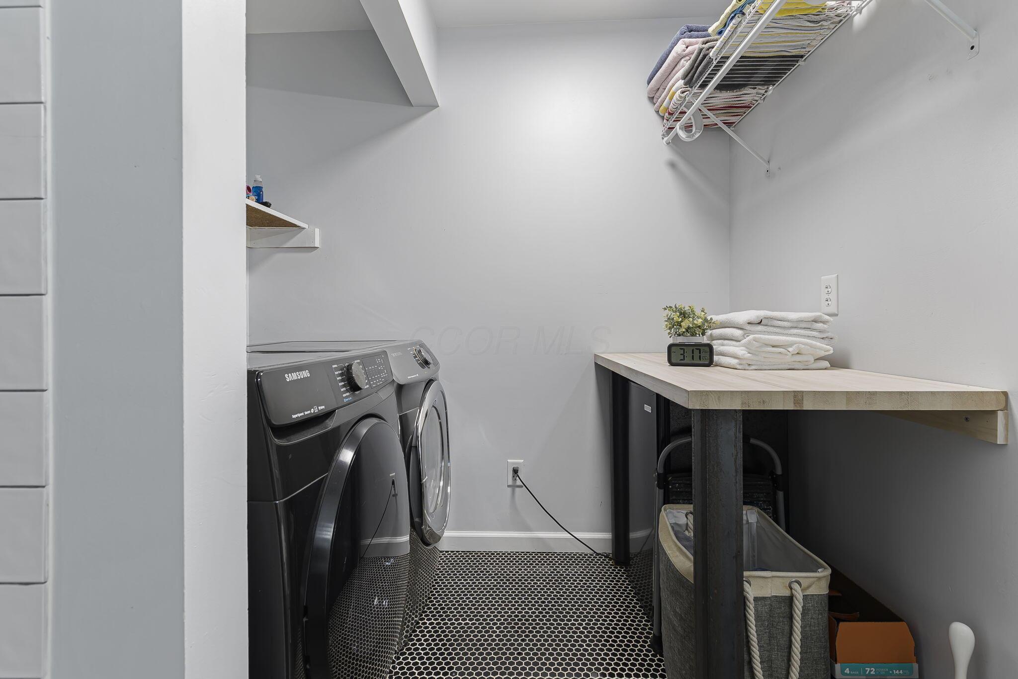 7140 Cook Road Powell, OH 43065 - Photo 71 of 87 Dedicated laundry room featuring front-load washer and dryer, quartz-finish countertop with integrated storage, geometric tile flooring, wall-mounted shelving, and recessed lighting throughout