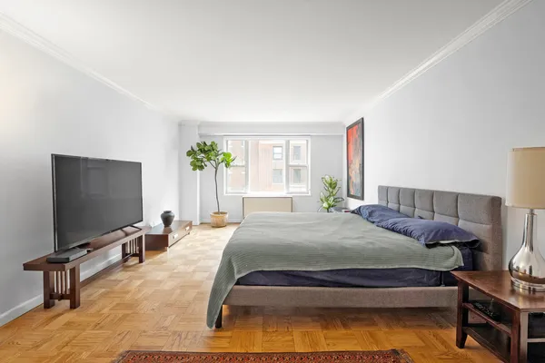 a bedroom with a bed television on desk and a window