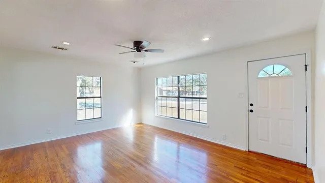 a view of an empty room with wooden floor and a window