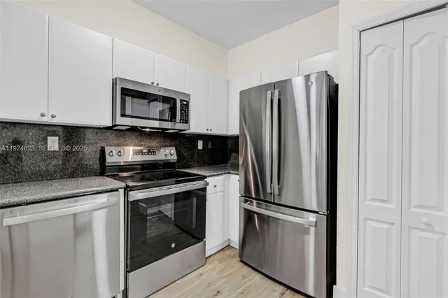 a kitchen with stainless steel appliances a refrigerator a sink and white cabinets