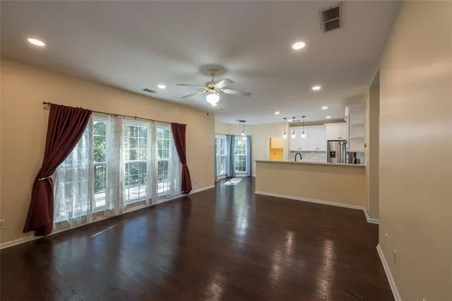 a view of an empty room with wooden floor and a kitchen